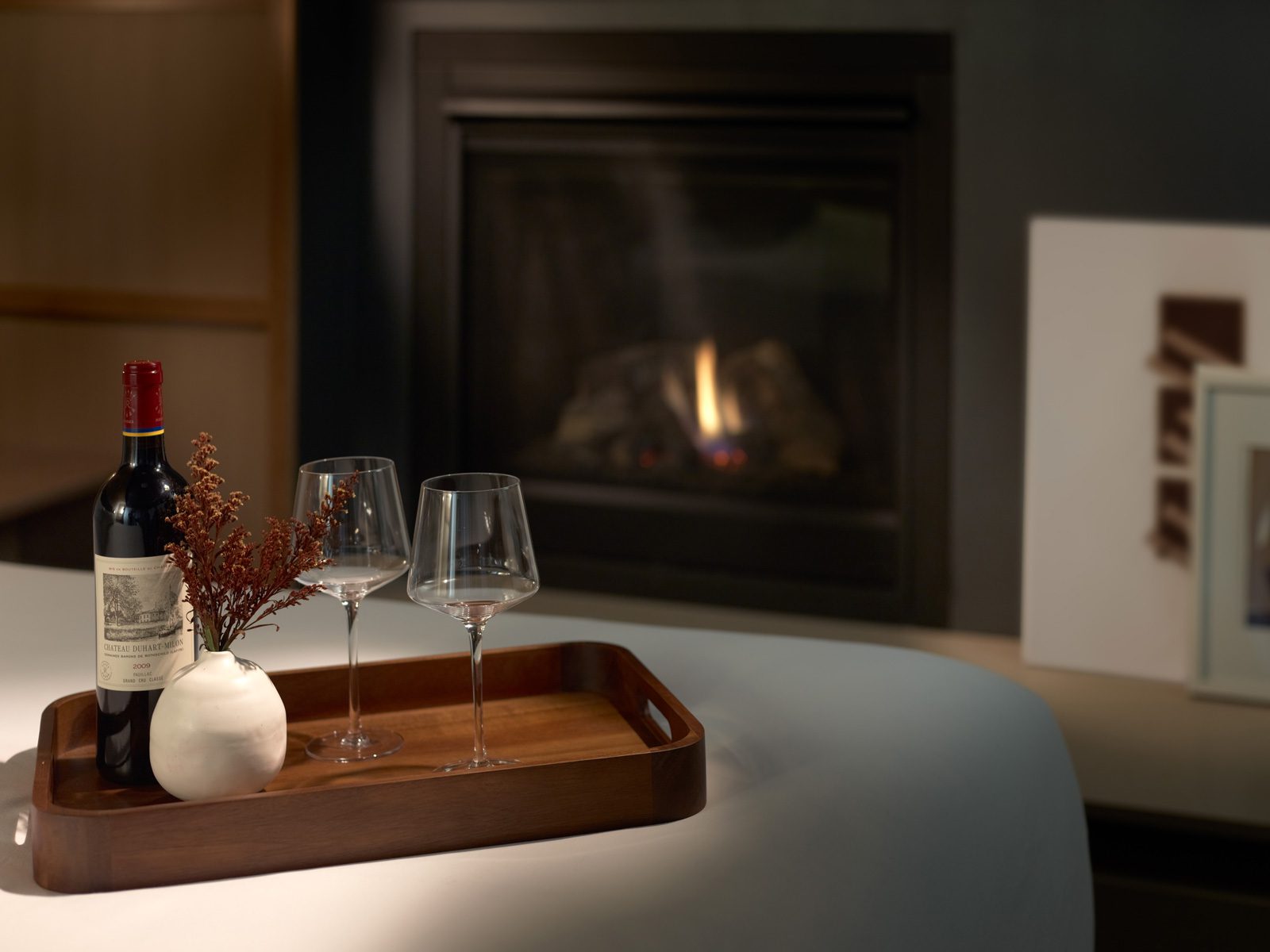 Harbor View King Fireplace and Wine Tray with wine and wineglasses on the bed with a fireplace in the background